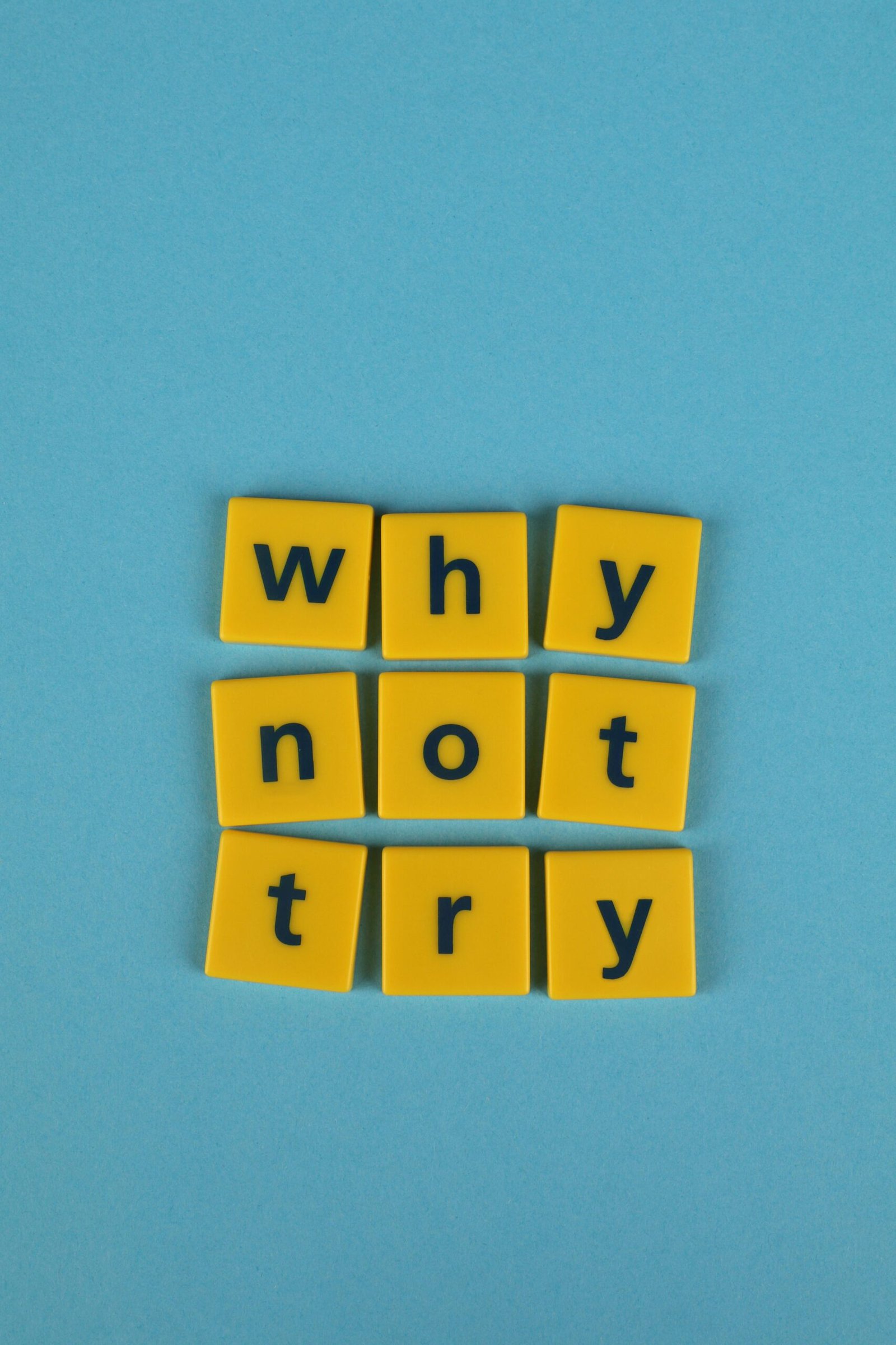 Inspiring message using yellow letter tiles on a blue background reading 'why not try'.