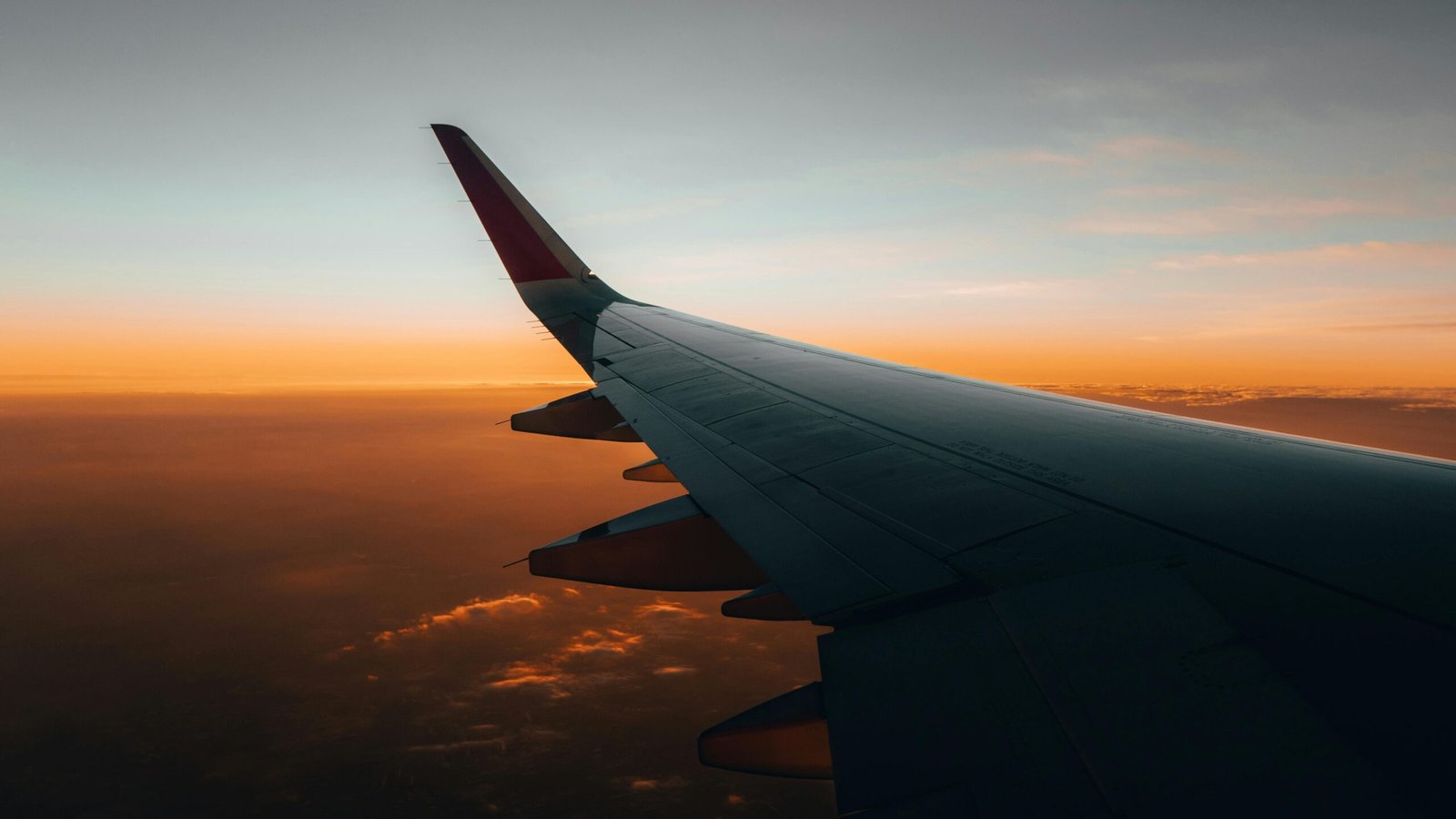 Stunning view of an airplane wing soaring above clouds during a vibrant sunrise.